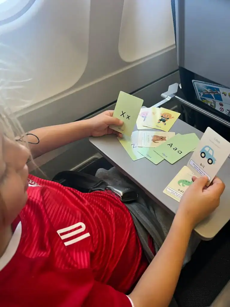Barn som spelar språklekar med kort på flygplansbordet.