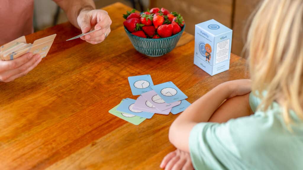 Barn spelar ett lärande spel med fruktkort och en vuxen på ett träbord.